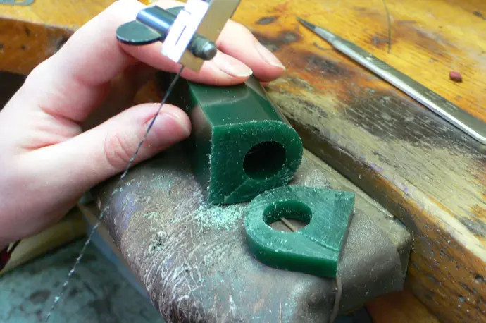 Main de la joaillière en train de scier un tube de cire pour les maquettes de bague