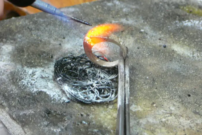 Main de la jaillière en train de souder une bague avec un chalumeau 