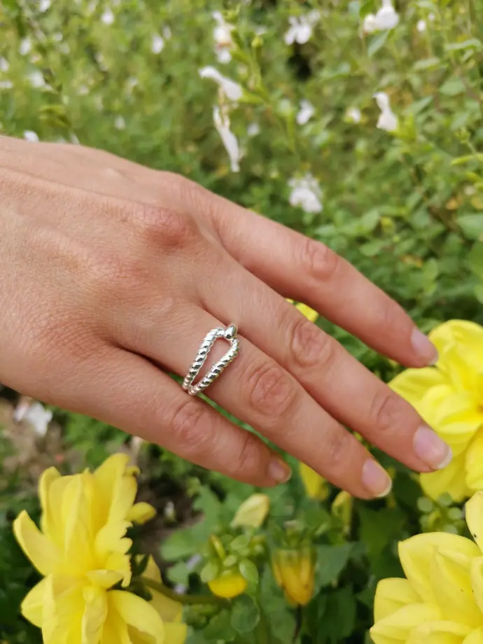 Une main portant une bague de la marque De Percin touche une fleur jaune