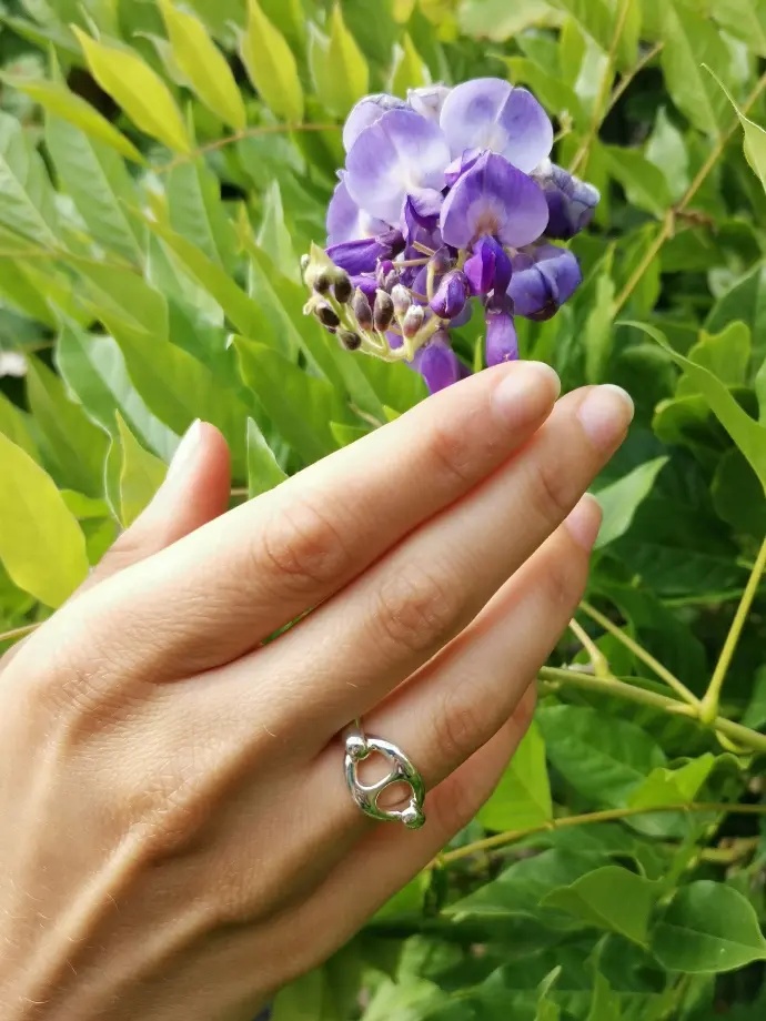 Une main portant une bague de la marque De Percin touche une fleur violette