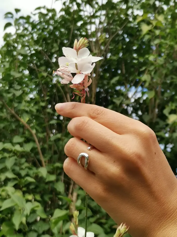 Une main portant une bague de la marque De Percin touche une fleur blanche