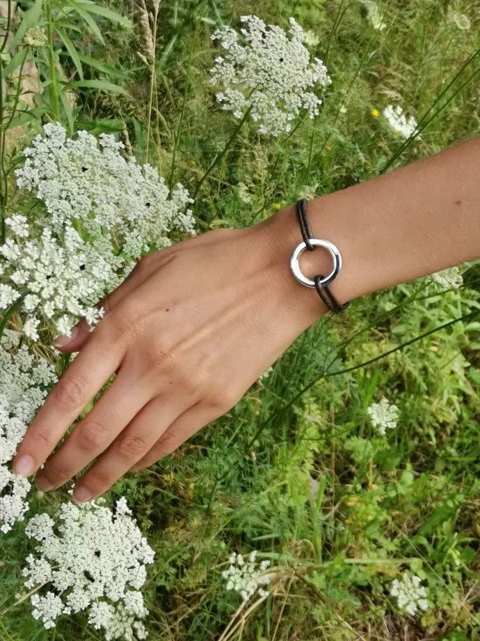 Une main portant un bracelet de la marque De Percin touche une fleur blanche